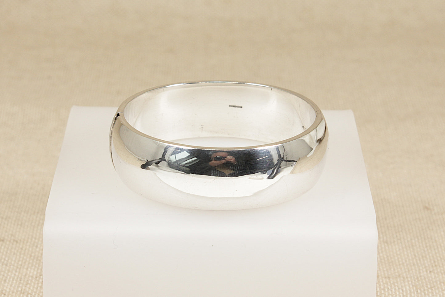 Silver hinged cuff bangle bracelet on a white stand with a beige background