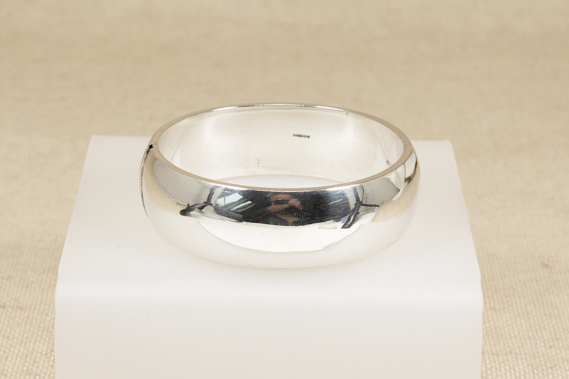 Silver hinged cuff bangle bracelet on a white stand with a beige background