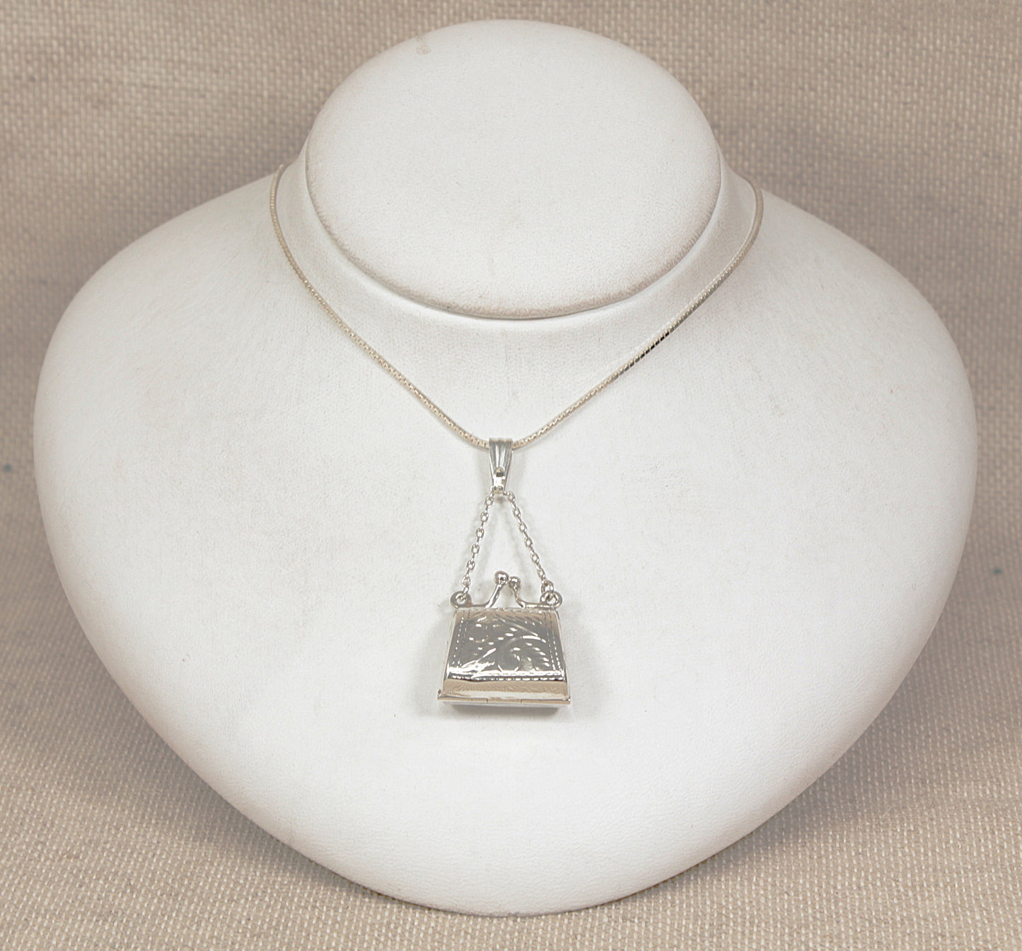 Silver necklace with a handbag locket  pendant on a white jewelry display