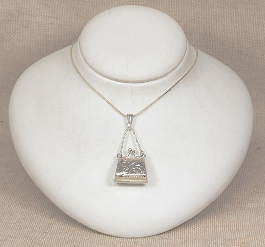 Silver necklace with a handbag locket  pendant on a white jewelry display