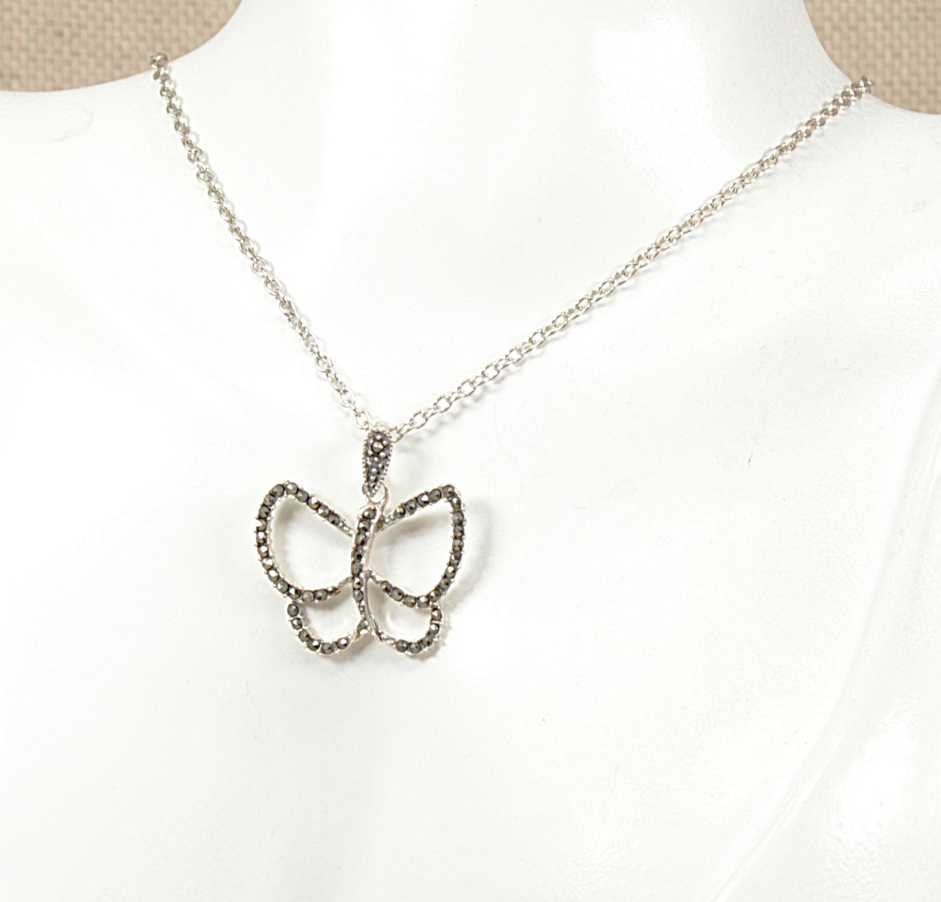 A silver butterfly pendant necklace displayed on a white mannequin bust. The necklace features a delicate silver chain and a butterfly-shaped pendant encrusted in sparkling marcasite  finish.