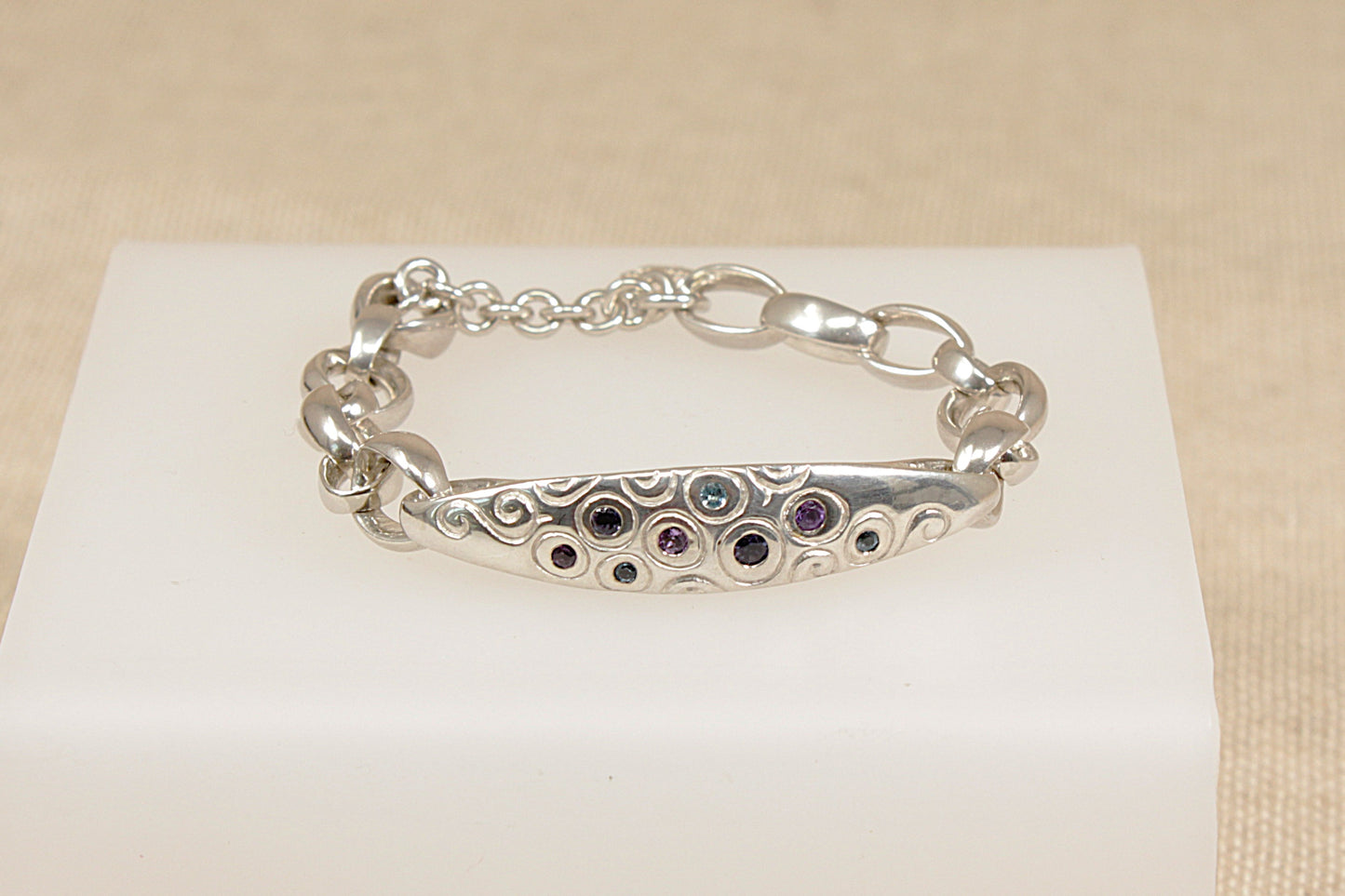 Silver bracelet with amethyst blue topaz and blue iolite gemstones on a white stand against a beige background