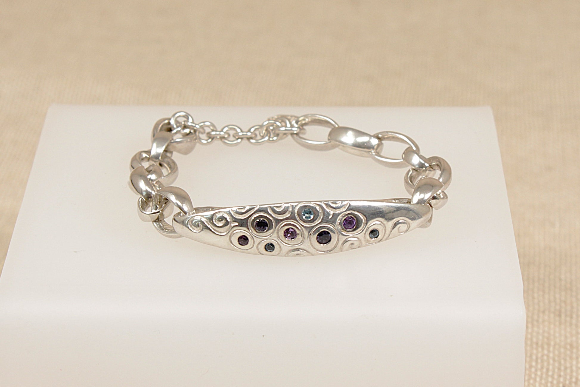 Silver bracelet with amethyst blue topaz and blue iolite gemstones on a white stand against a beige background
