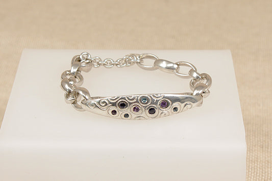 Silver bracelet with amethyst blue topaz and blue iolite gemstones on a white stand against a beige background