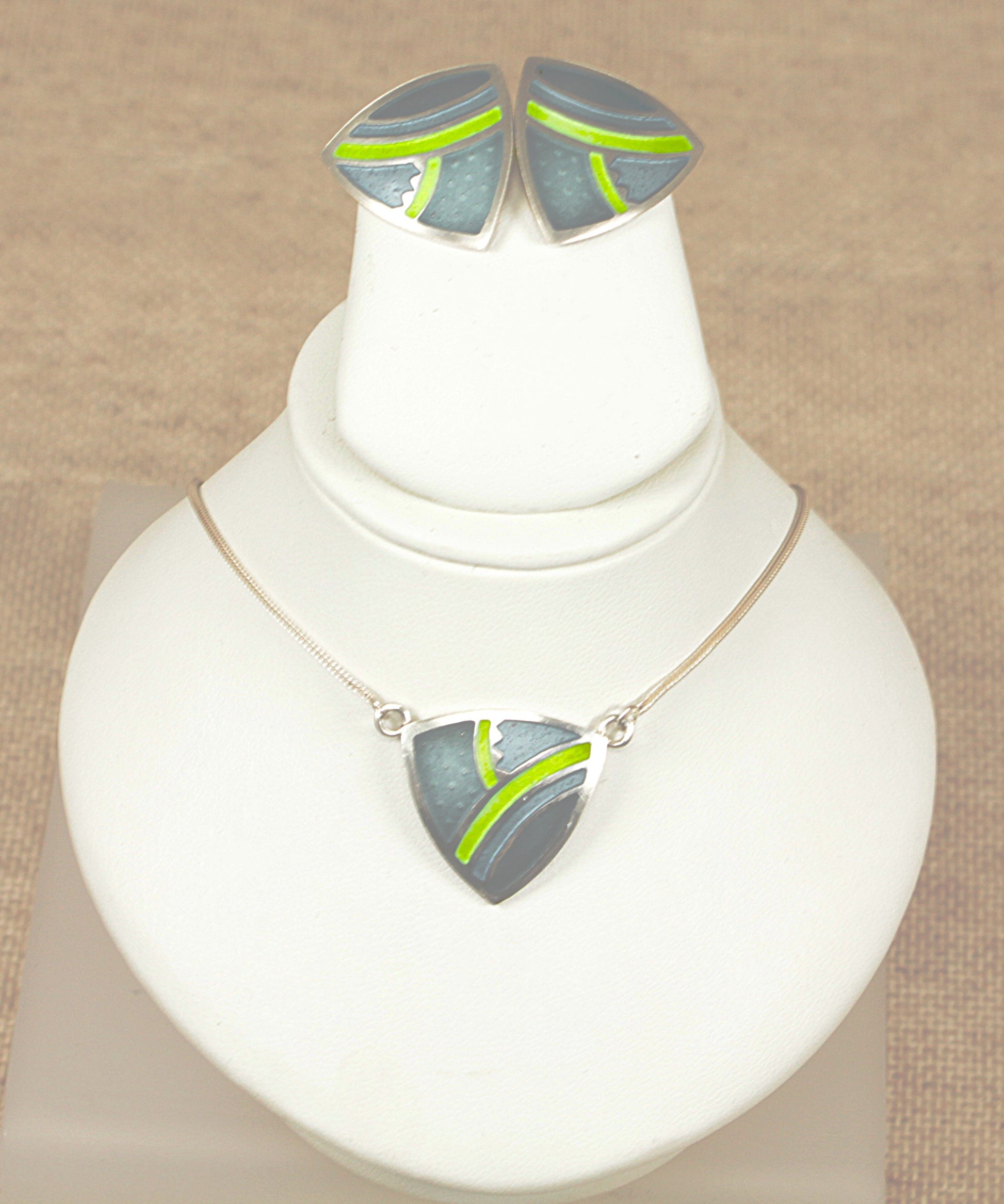Jewelry set with necklace and earrings on a white stand against a beige background