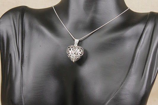 A silver filigree heart pendant necklace displayed on a black mannequin bust against a light beige background.