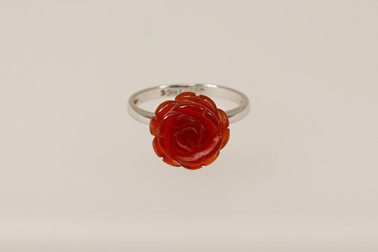 A silver ring with a carved red stone in the shape of a rose as the central element on a white background.