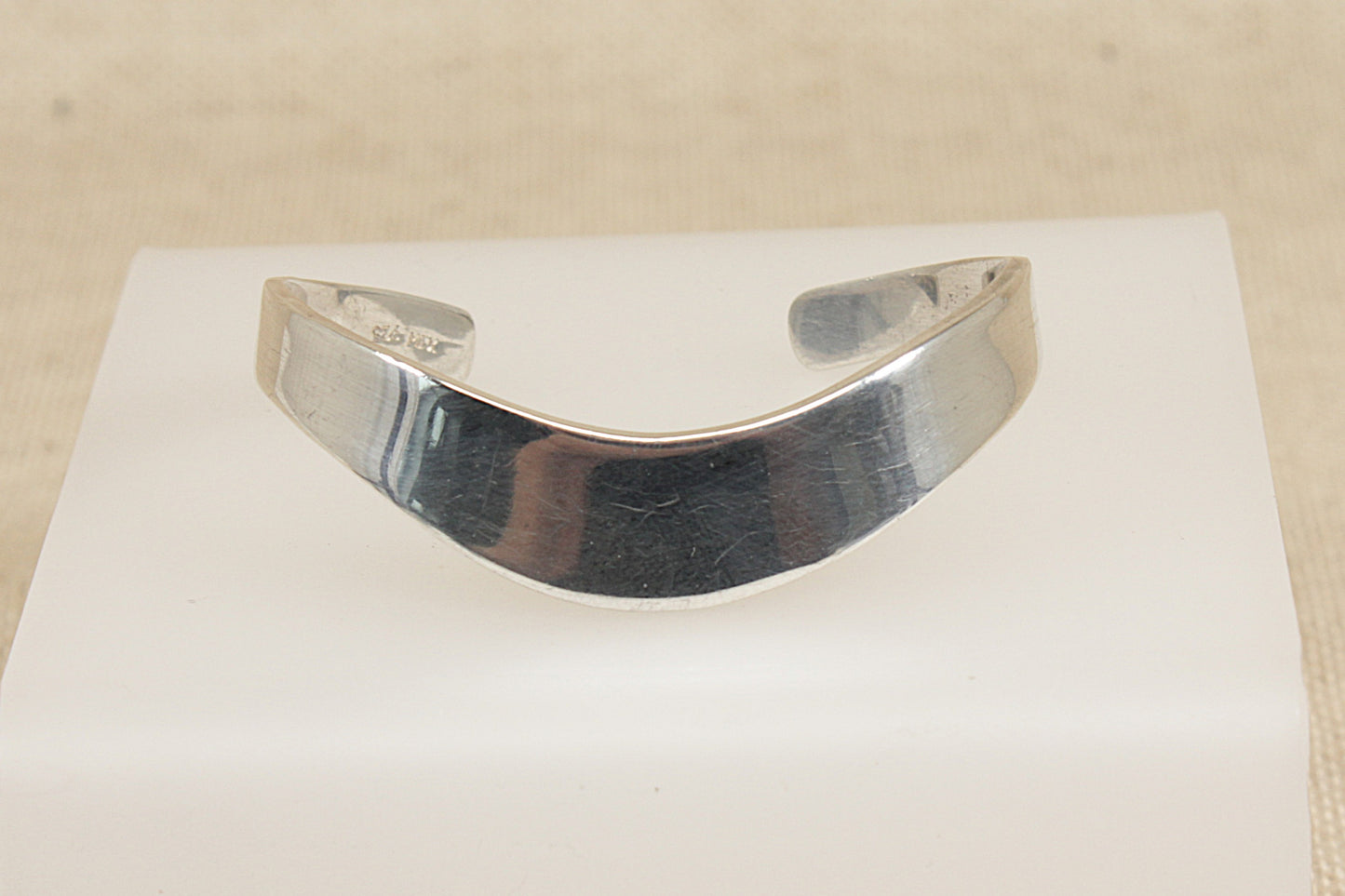 Silver bracelet on a white card with a beige background
