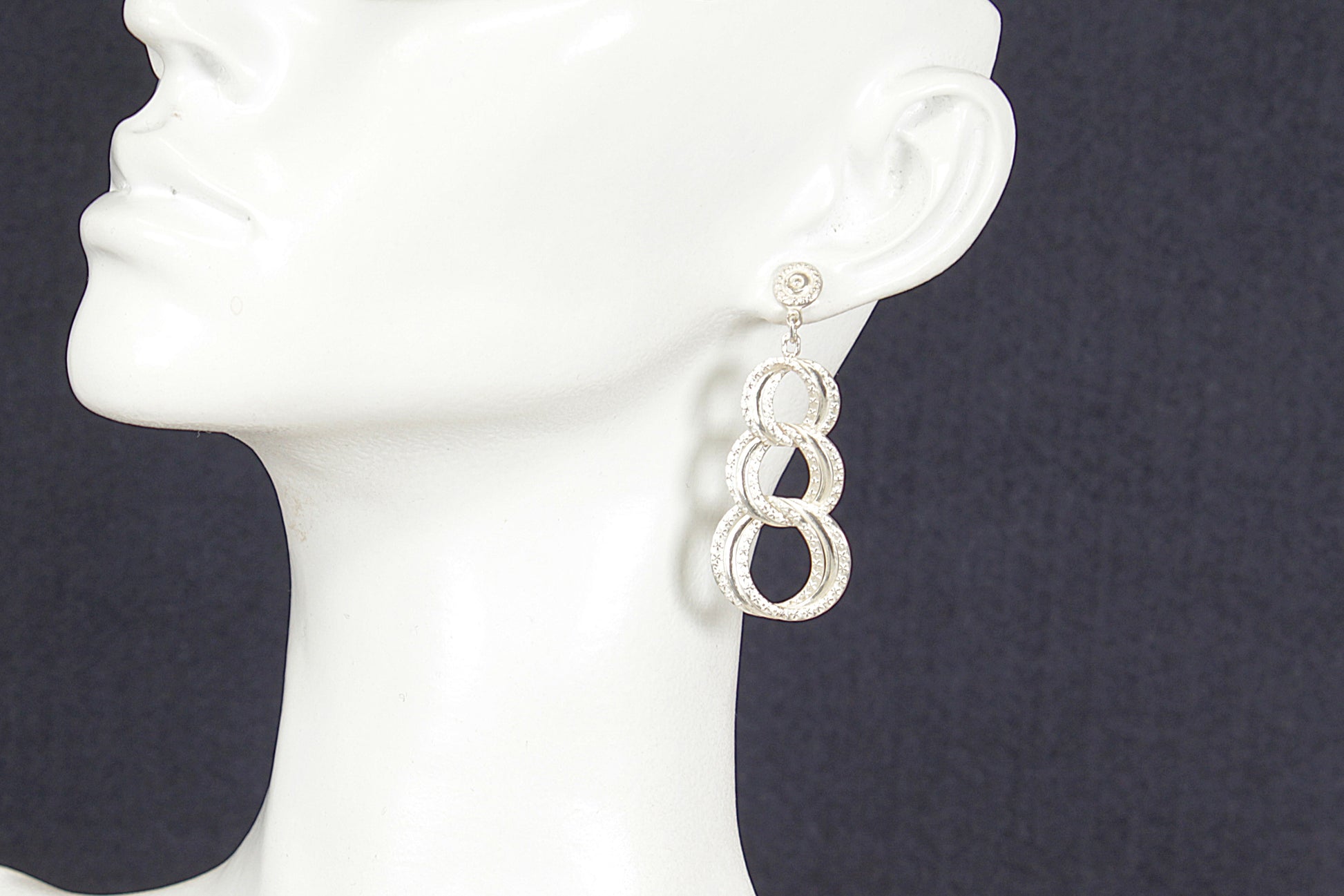 Silver earrings on a white mannequin head against a dark background