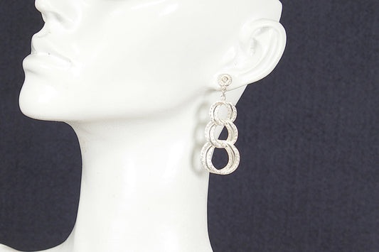 Silver earrings on a white mannequin head against a dark background