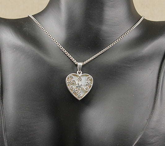 A silver heart-shaped reversible pendant necklace with an intricate filigree design, displayed on a black mannequin bust.