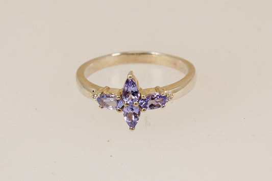 A silver ring featuring four marquise-cut purple iolite gemstones on a plain light beige background.
