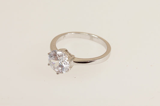 Silver solitaire ring with a clear cubic zirconia gemstone on a beige background