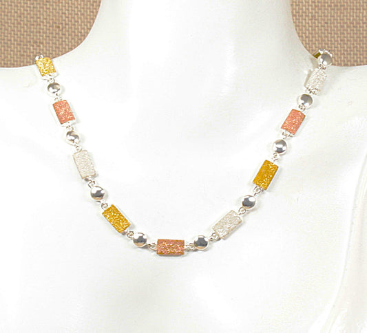 A silver necklace with rectangular silver gilt links in yellow, orange, and white, displayed on a white mannequin bust.