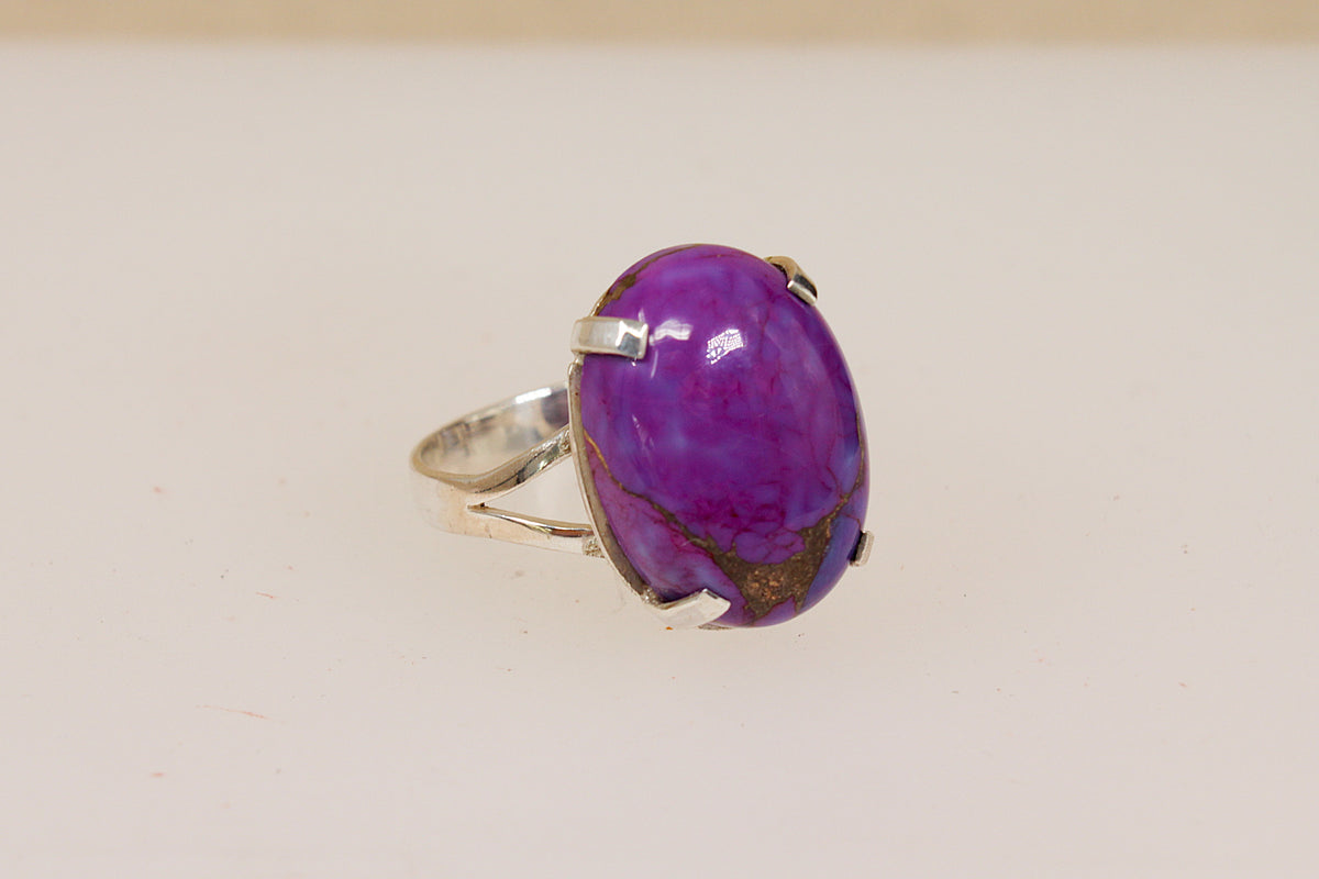 A silver ring featuring a large, oval purple agate stone with natural brown veining, set in a prong setting on a plain light background.