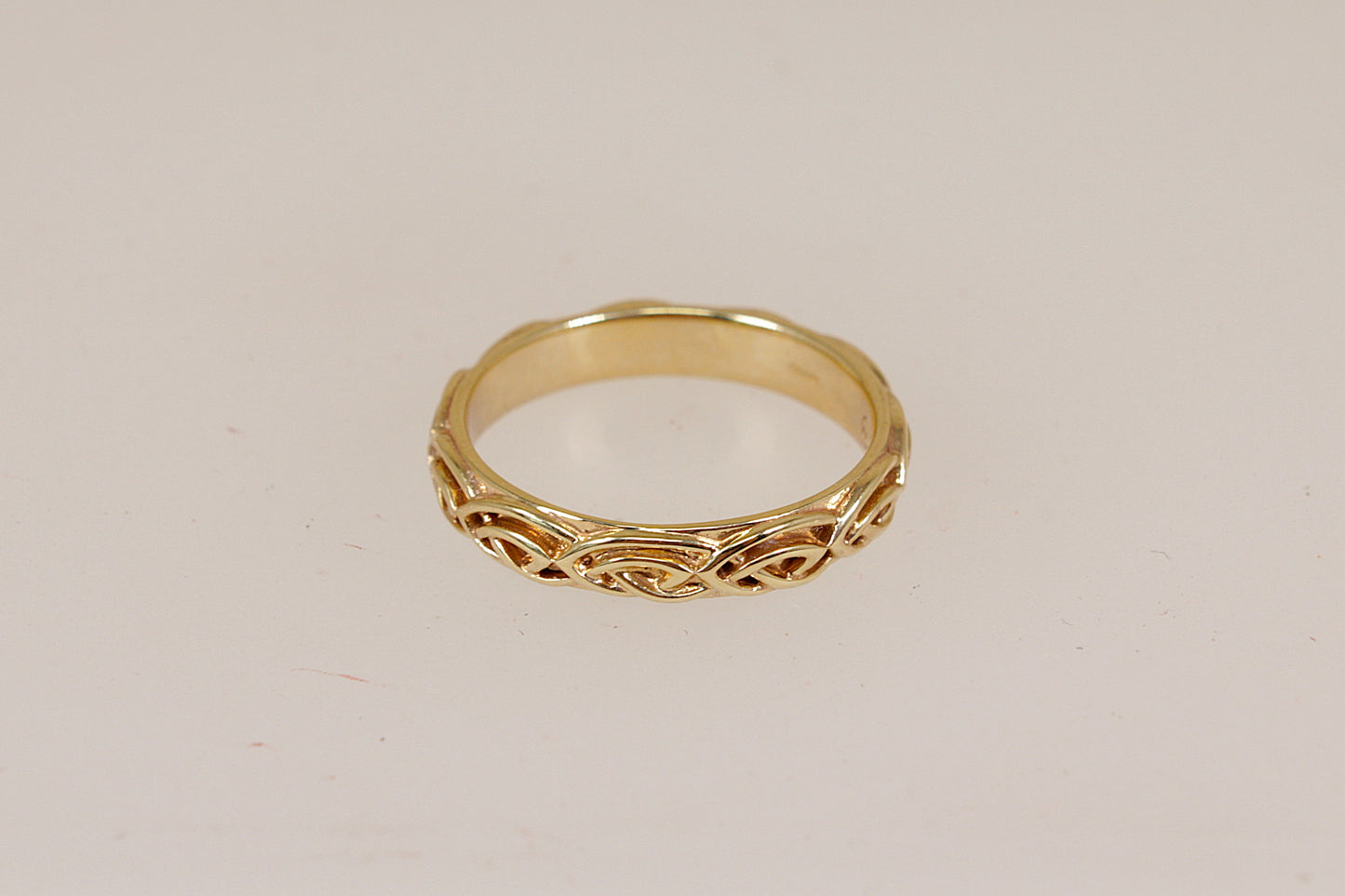 A yellow gold Annwyl band ring by Clogau with an intricate celtic pattern, shown on a plain light beige background.