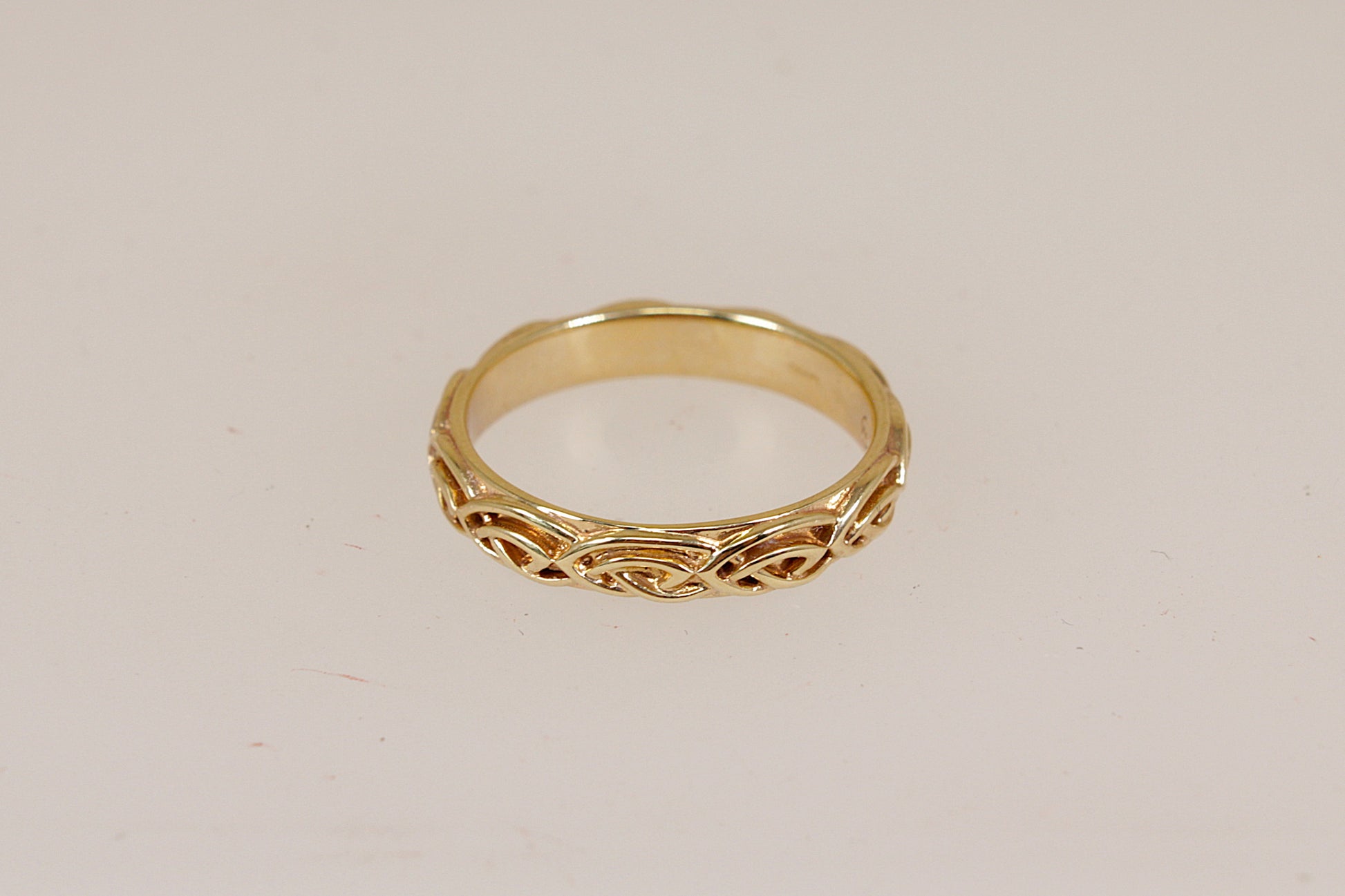 A yellow gold Annwyl band ring by Clogau with an intricate celtic pattern, shown on a plain light beige background.