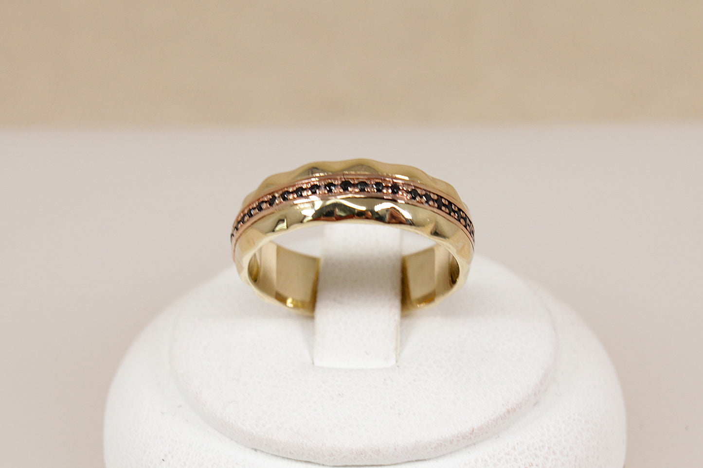 A yellow gold band ring featuring a textured, scalloped outer edge and a channel-set row of small round blue sapphire gemstones, shown on a plain light beige background.