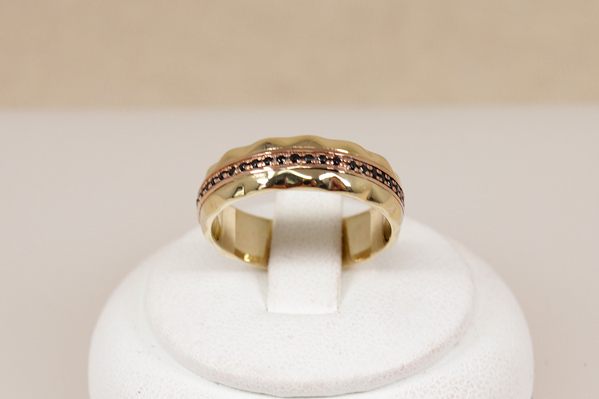 A yellow gold band ring featuring a textured, scalloped outer edge and a channel-set row of small round blue sapphire gemstones, shown on a plain light beige background.