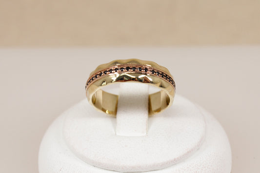 A yellow gold band ring featuring a textured, scalloped outer edge and a channel-set row of small round blue sapphire gemstones, shown on a plain light beige background.