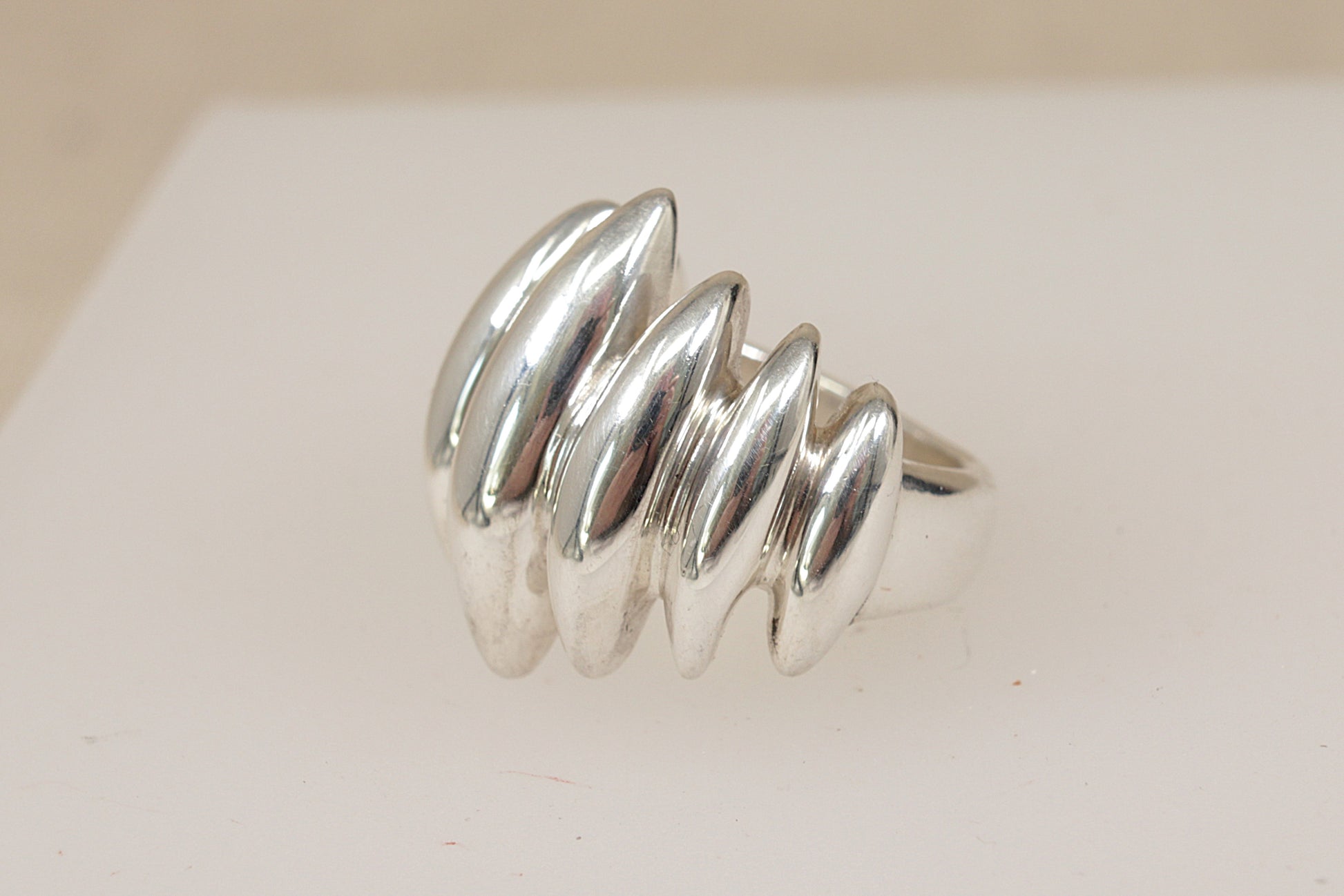 A vintage danish design sterling silver brutalist ring with a wavy, segmented design, displayed on a white jewelry stand against a soft beige background.