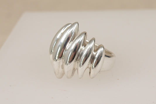 A vintage danish design sterling silver brutalist ring with a wavy, segmented design, displayed on a white jewelry stand against a soft beige background.