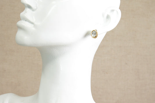 A close-up side view of a white mannequin bust wearing a yellow gold blue topaz stud earring, set against a neutral beige background.
