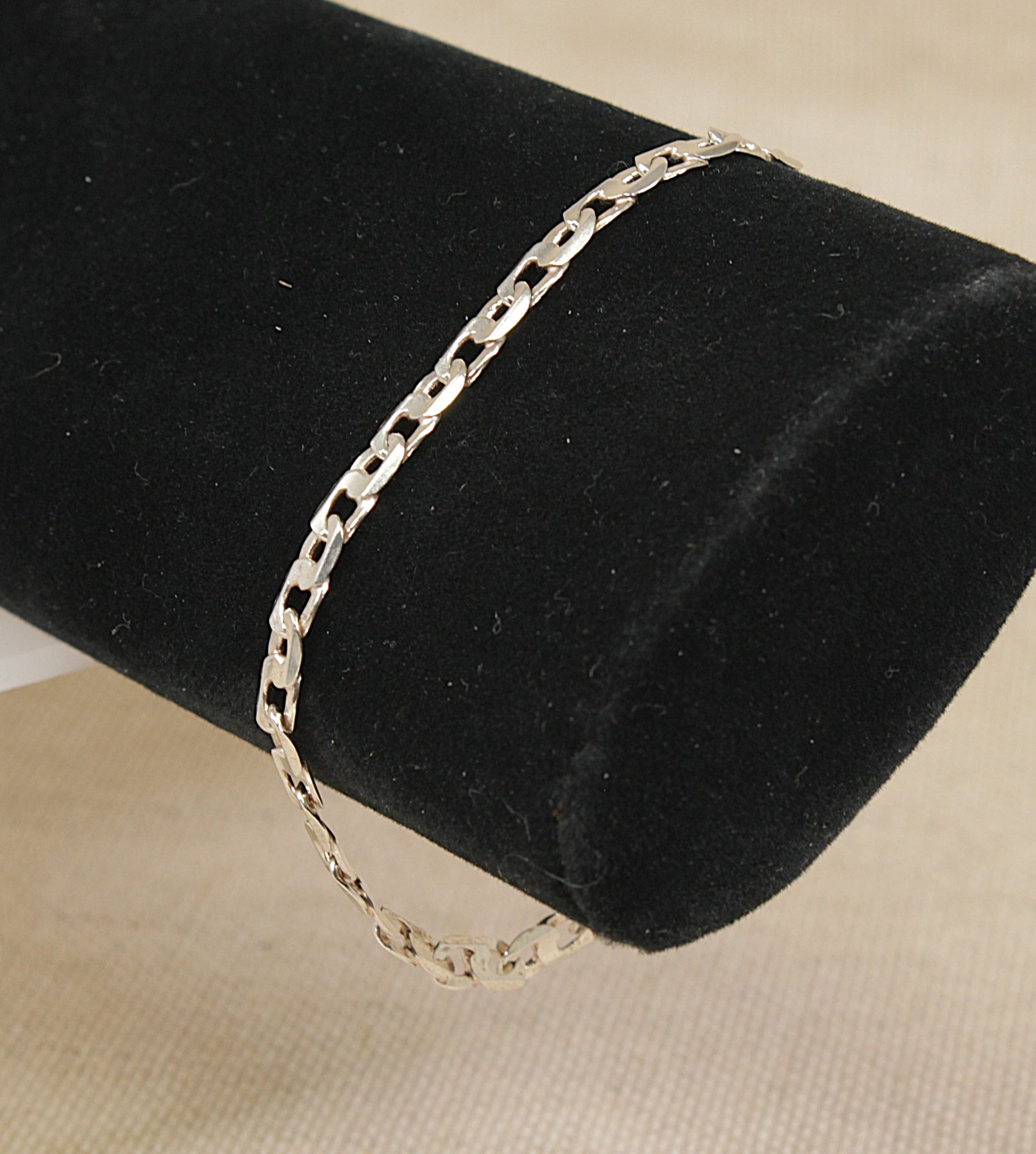 A silver curb link bracelet with a lobster clasp, displayed on a black bracelet stand.