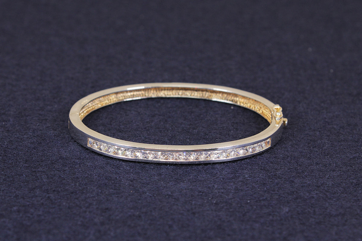 A sterling silver hinged bangle bracelet with a row of clear pavé-set cz gemstones on the front, displayed on a dark textured background.
