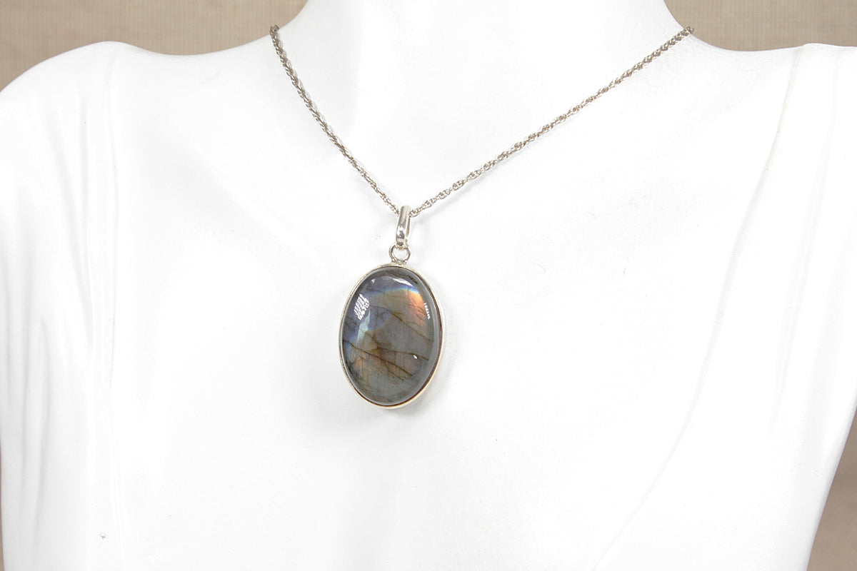 A silver chain necklace with an oval labradorite gemstone pendant, displayed on a white mannequin bust.