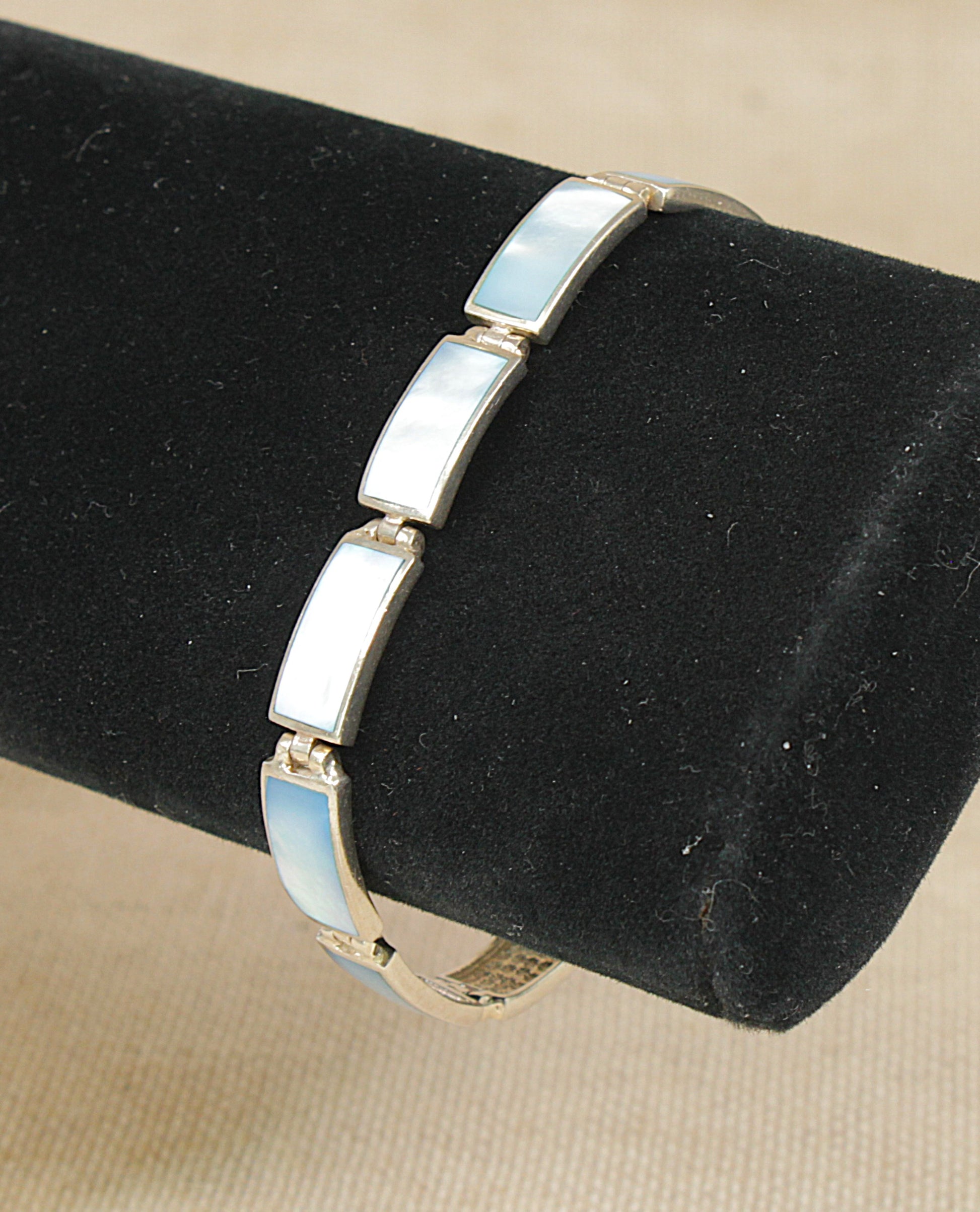 A sterling silver bangle bracelet with rectangular mother of pearl inlay panels, displayed on a black cylindrical jewelry stand against a beige fabric background.