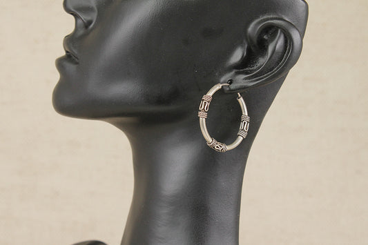 A pair of sterling silver Suarti style hoop earrings with textured vertical bands, shown on a black mannequin head against a light beige background.