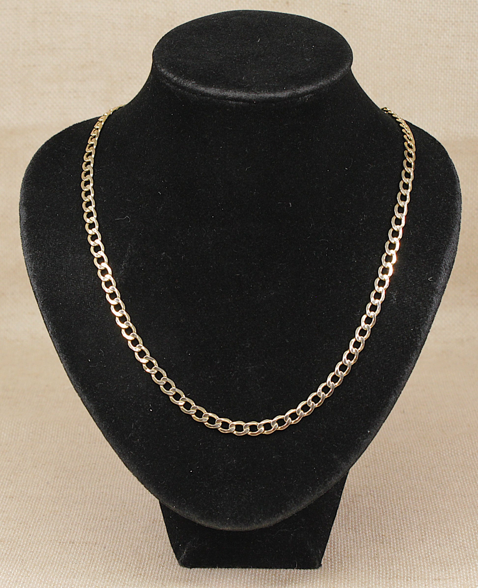A bonded 9ct gold and sterling silver  curb link chain necklace displayed on a black velvet jewelry bust against a light beige textured background.