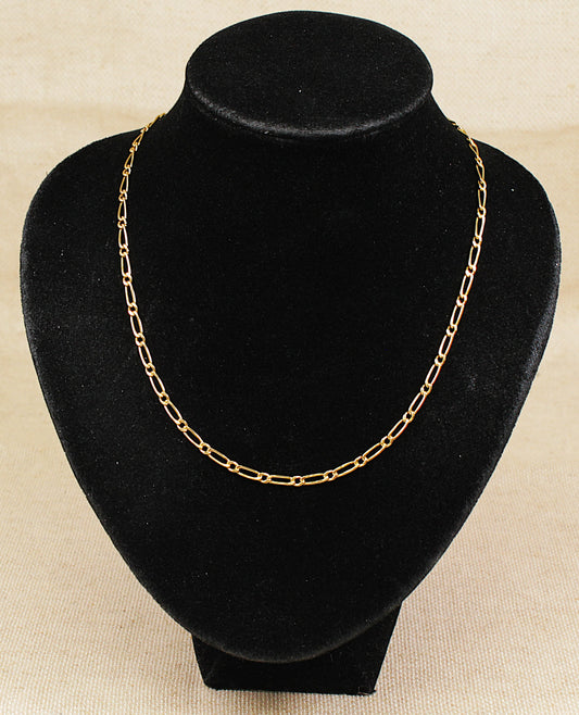 A gold oval link necklace chain displayed on a black bust with a beige background 