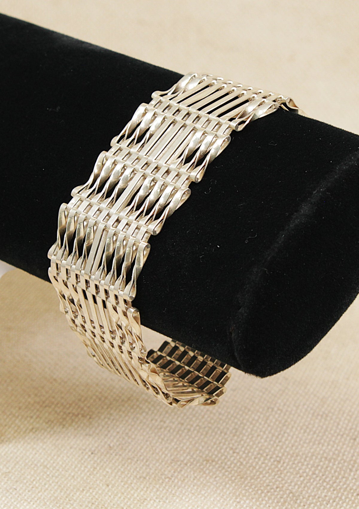 A silver link gate  bracelet displayed on a black cylindrical jewelry stand against a light beige fabric background.