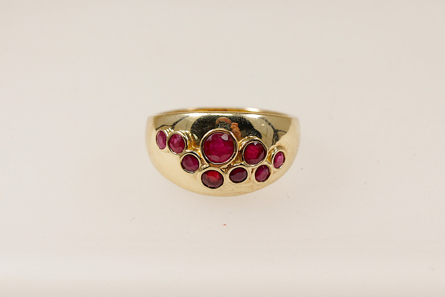 A vintage 9ct yellow gold ruby scatter ring featuring nine bezel set ruby gemstones scattered across the head of the ring, the ring has full Birmingham hallmarks with the date letter for 1984, UK finger size O.