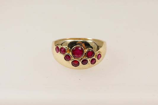A vintage 9ct yellow gold ruby scatter ring featuring nine bezel set ruby gemstones scattered across the head of the ring, the ring has full Birmingham hallmarks with the date letter for 1984, UK finger size O.
