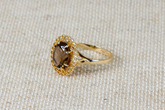 This beautiful 9ct Gold ring is set with an oval Smoky Quartz in a 8 claw setting, The finely made decorative setting has tiny heart shapes amongst the scrollwork, The ring is made in the traditional richness of yellow gold, It is in excellent condition and inside the band it has Edinburgh hallmarks Goldsmiths mark for Charles Lucas &amp; Sons, UK Finger size: Q.