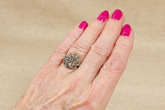 Hand wearing a silver marcasite decorative ring with pink nail polish on a beige background