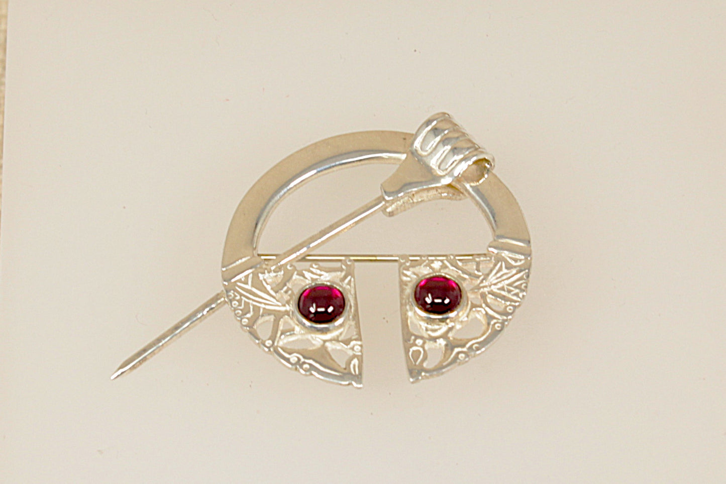 Silver brooch with red garnet gemstones on a beige background