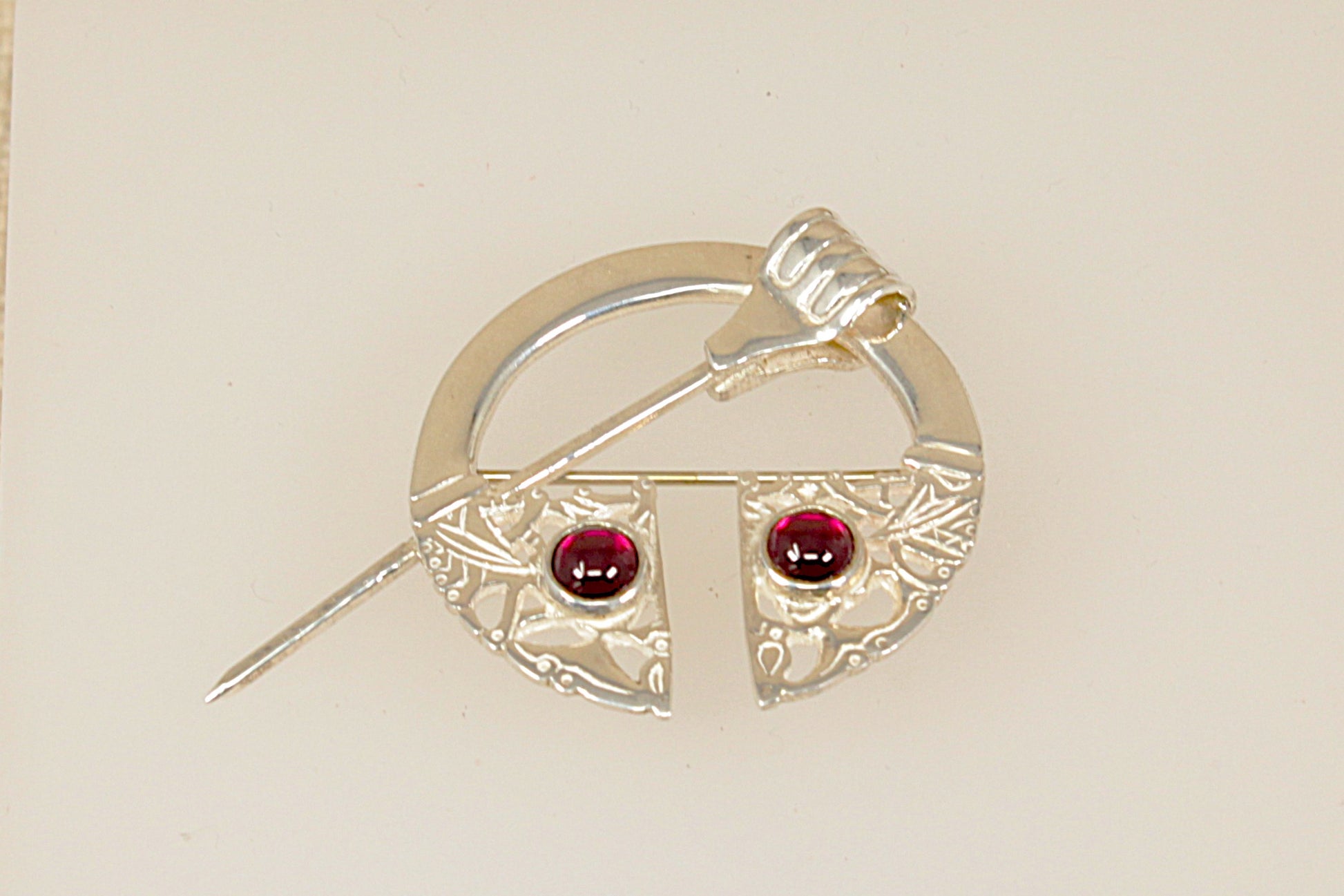Silver brooch with red garnet gemstones on a beige background