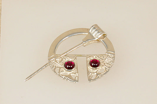 Silver brooch with red garnet gemstones on a beige background