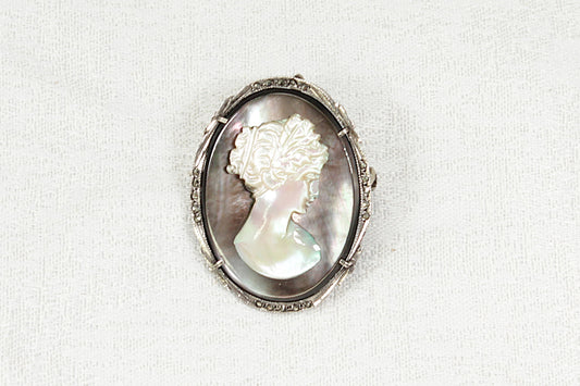 Cameo brooch with a carved mother of pearl woman's face in a silver and marcasite oval frame on a white background