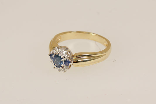 9ct Gold Sapphire and Diamond Cluster Ring, A beautiful and distinctive 9ct Gold ring, showcasing an interesting and elegant design. At its heart is a vibrant oval Blue Sapphire, flanked by two round Blue Sapphires, forming a rich and regal trilogy centrepiece. it bears full London hallmarks for 1993, confirming its gold purity and vintage authenticity, perfect as a unique engagement ring, UK Finger size: O.