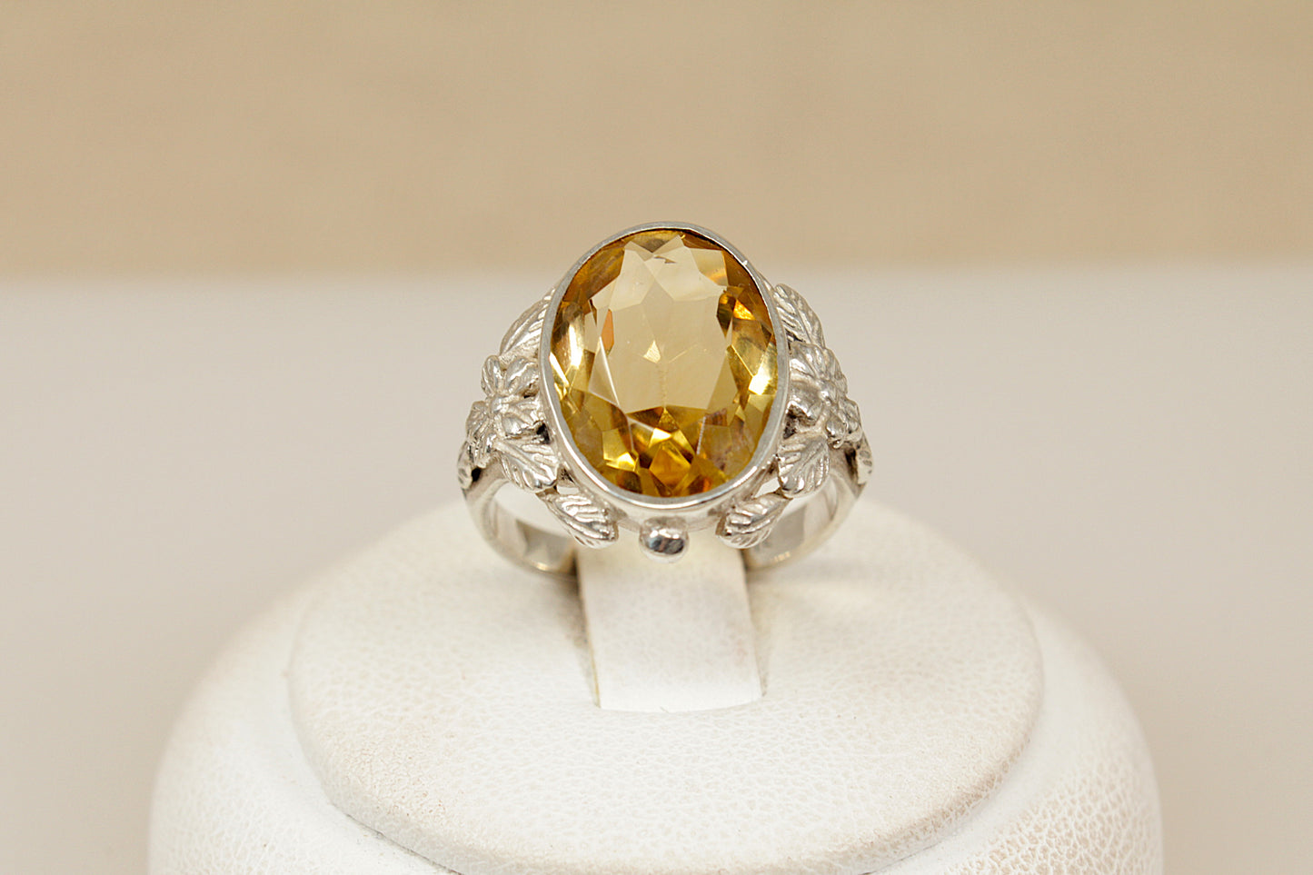 Decarative silver ring with a citrine gemstone on a white stand against a beige background