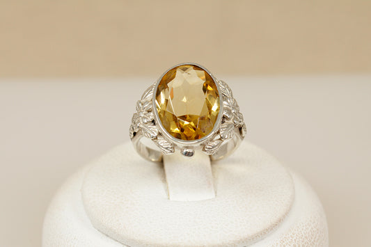 Decarative silver ring with a citrine gemstone on a white stand against a beige background