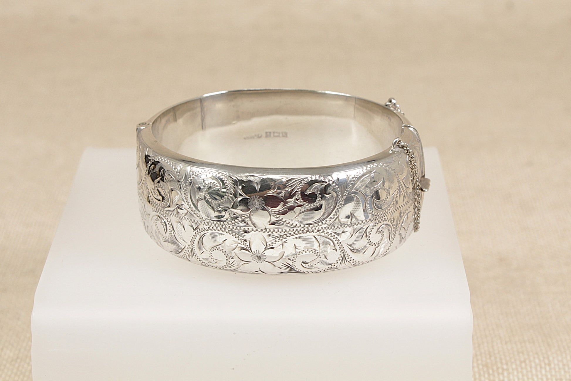 Vintage Silver bracelet cuff bangle with intricate designs on a white stand against a beige background