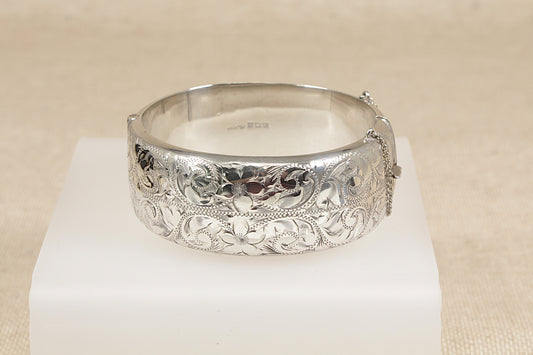 Vintage Silver bracelet cuff bangle with intricate designs on a white stand against a beige background