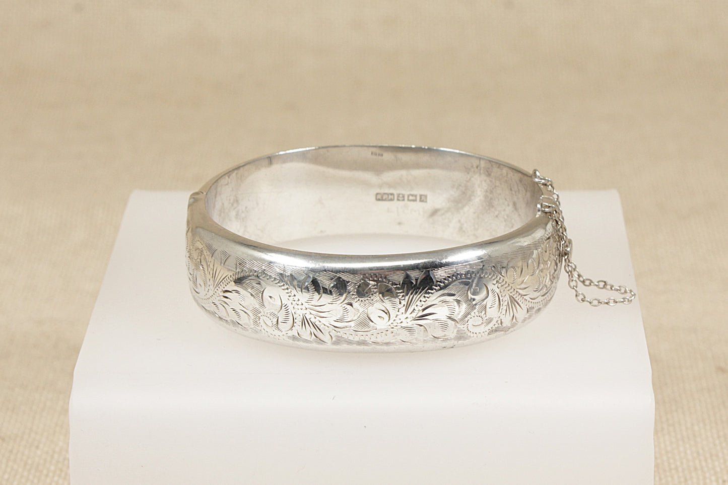 Silver bracelet bangle with intricate designs on a white stand against a beige background
