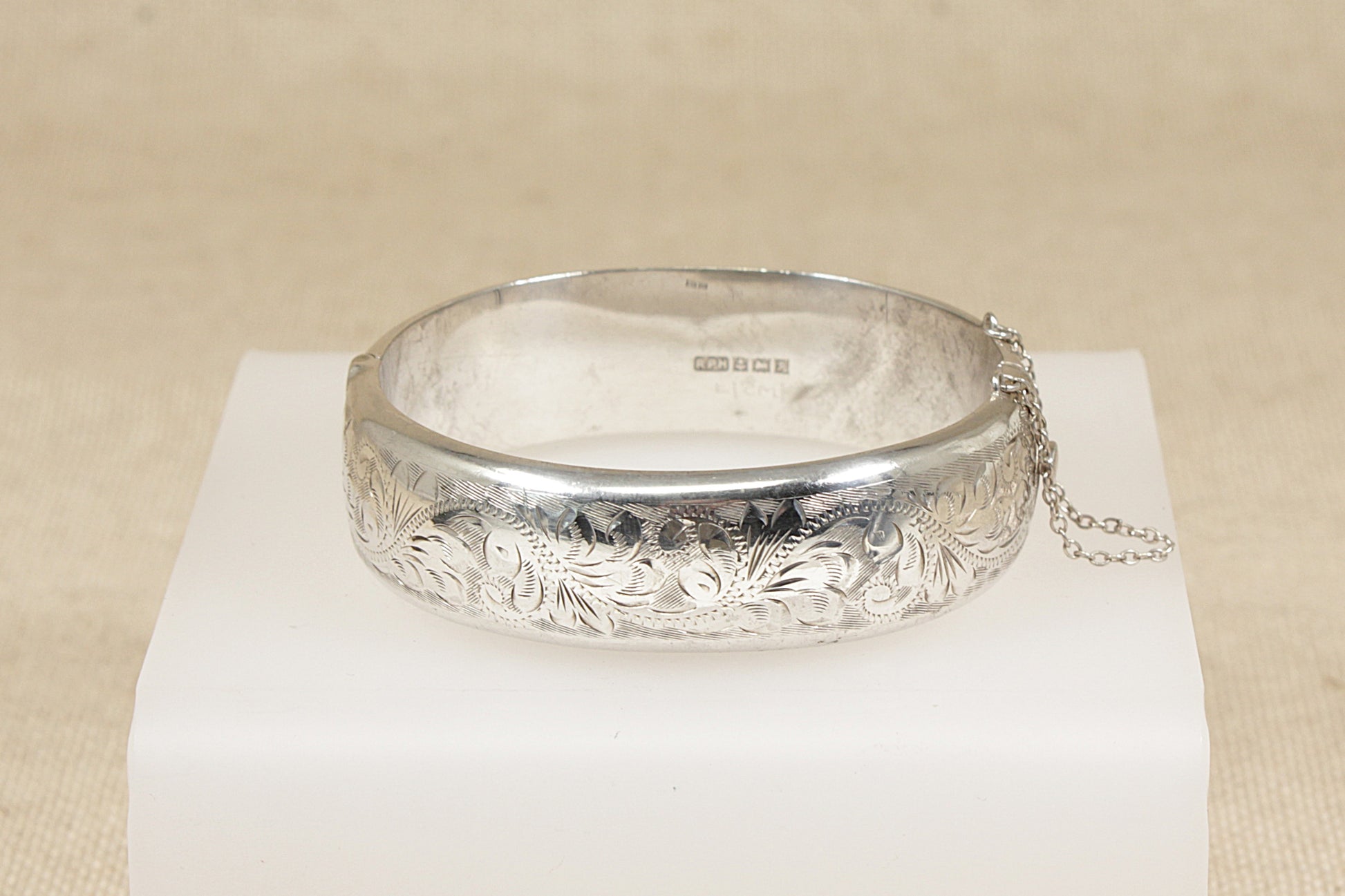 Silver bracelet bangle with intricate designs on a white stand against a beige background